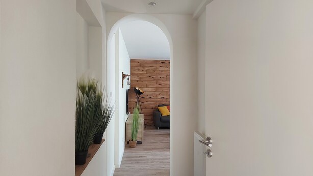 Een gang met een witte boog die leidt naar een woonkamer met een houten wand, een bank en een lamp.