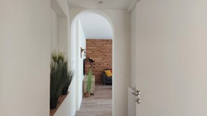 Un pasillo con un arco blanco que conduce a una sala de estar con pared de madera, un sofá y una lámpara.