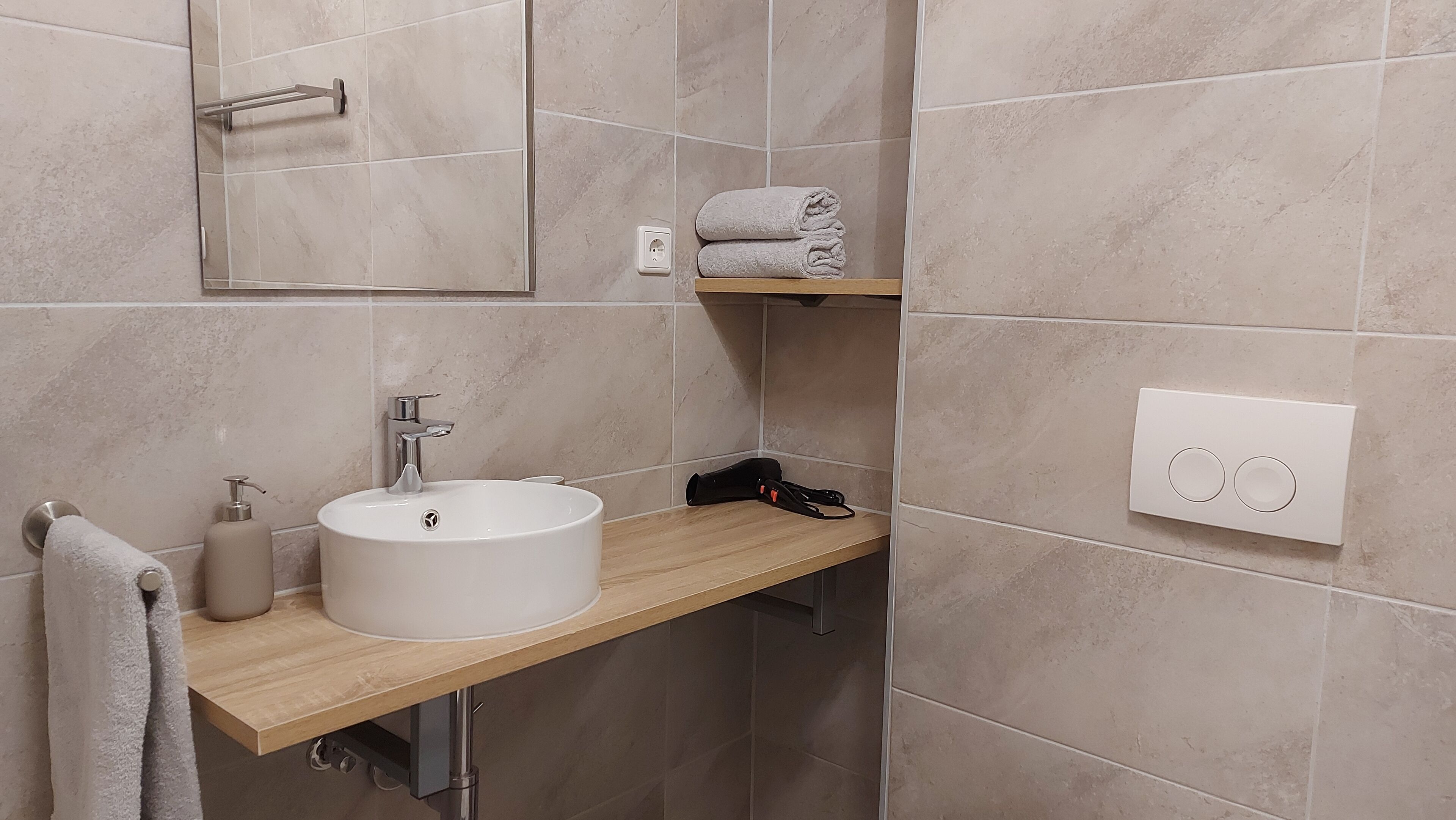 A bathroom with a white sink, a mirror, a towel rack, and a towel shelf.
