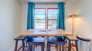 Een eethoek met een houten tafel en vier stoelen, een raam met blauwe gordijnen en een vloerlamp.