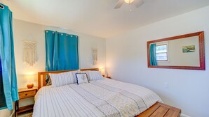 Een slaapkamer met een bed, een houten bankje, een plafondventilator en een spiegel aan de muur.