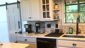 A kitchen with white cabinets, a dishwasher, a coffee maker, and a window with a view of greenery.