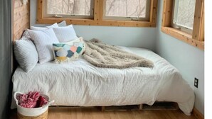 Une chambre à coucher avec un lit, deux fenêtres, un plafond en bois et un mur en pierre.