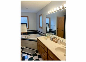 A bathroom with a double sink, a bathtub, and a large mirror with lights.