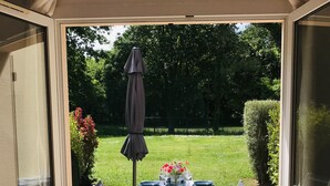 Une terrasse avec une table dressée pour deux personnes, un parasol et une vue sur un jardin.