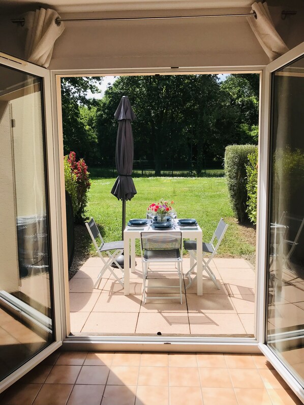 Eine Terrasse mit Tisch für zwei Personen, einem Sonnenschirm und Blick auf einen Garten.