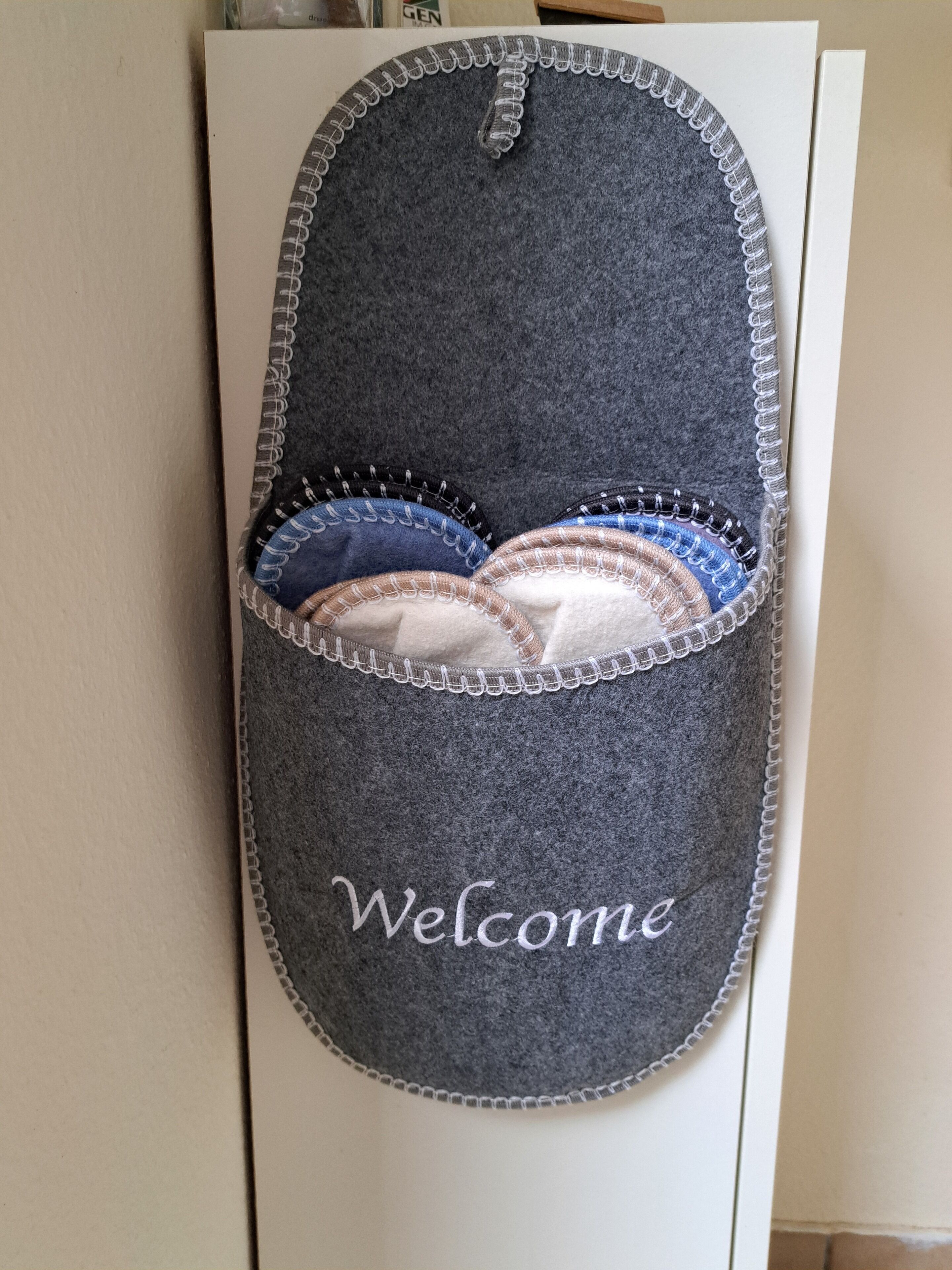 A gray slipper with a 'Welcome' embroidered on it, placed on a white surface.
