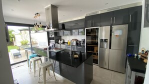 A modern kitchen with a central island, stainless steel appliances, and a view of the outdoors. - ANGLET, 8 pers COAST HOUSE WITH SWIMMING POOL, NEAR THE BEACH, cycle path, GOLF (Anglet)
