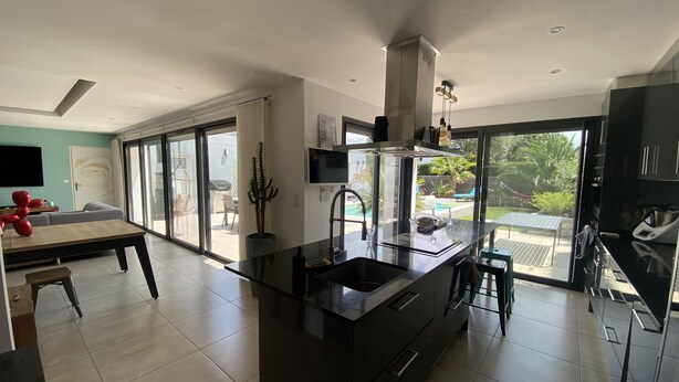 A modern kitchen with a central island, large windows, and a view of the outdoors. - ANGLET, 8 pers COAST HOUSE WITH SWIMMING POOL, NEAR THE BEACH, cycle path, GOLF (Anglet)