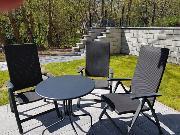 En udendørs terrasse med et rundt bord og tre stole.