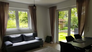 Un salon moderne avec un canapé gris, une table à manger avec des chaises et de grandes fenêtres dotées de rideaux.