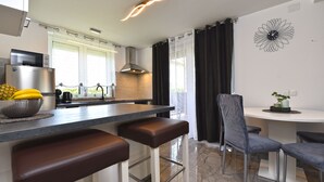 A modern kitchen with a central island, bar stools, a dining area with a chair, and a decorative wall clock.