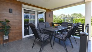 A modern outdoor dining area with a table and chairs, a potted plant, and a view of the greenery and buildings in the background.