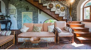 A cozy living room with a stone wall, a wooden staircase, and a large window. - Rocca Angelica - Villa with swimming pool, 40 min far from Positano (Santa Maria del Castello)
