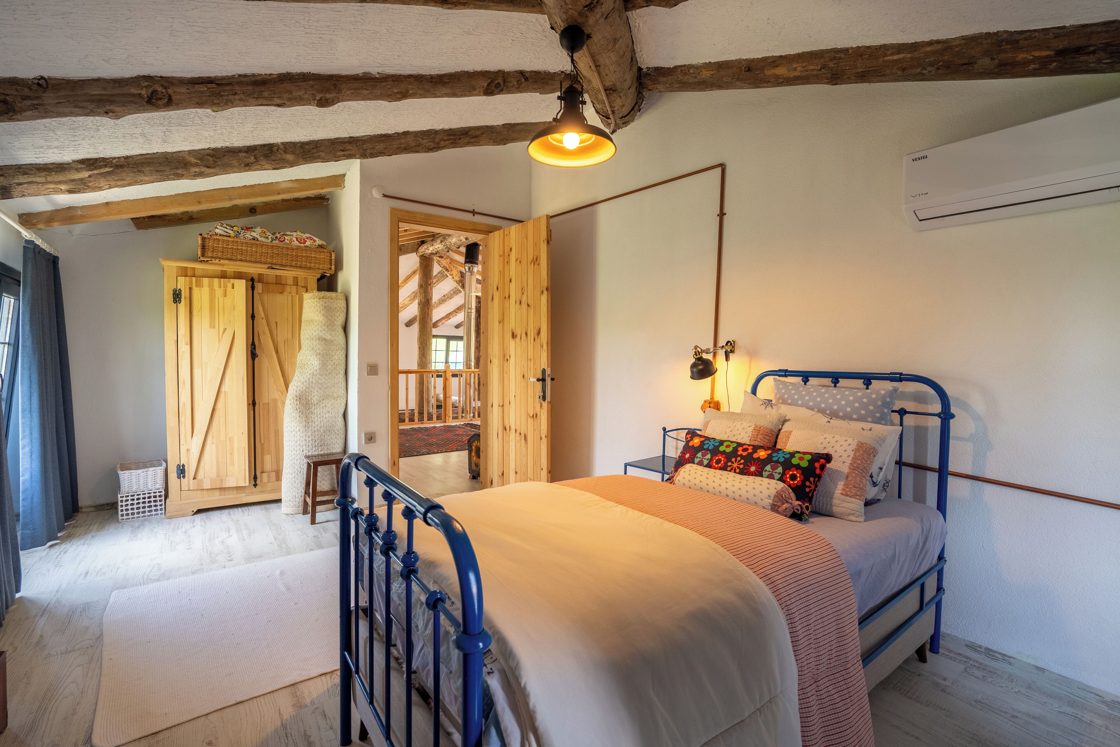 Un dormitorio con techo de madera, una cama con estructura metálica azul y un ventanal grande.
