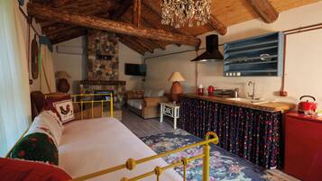 A cozy room with a bed, a stone fireplace, a wooden ceiling, and a kitchen area with a red fridge.
