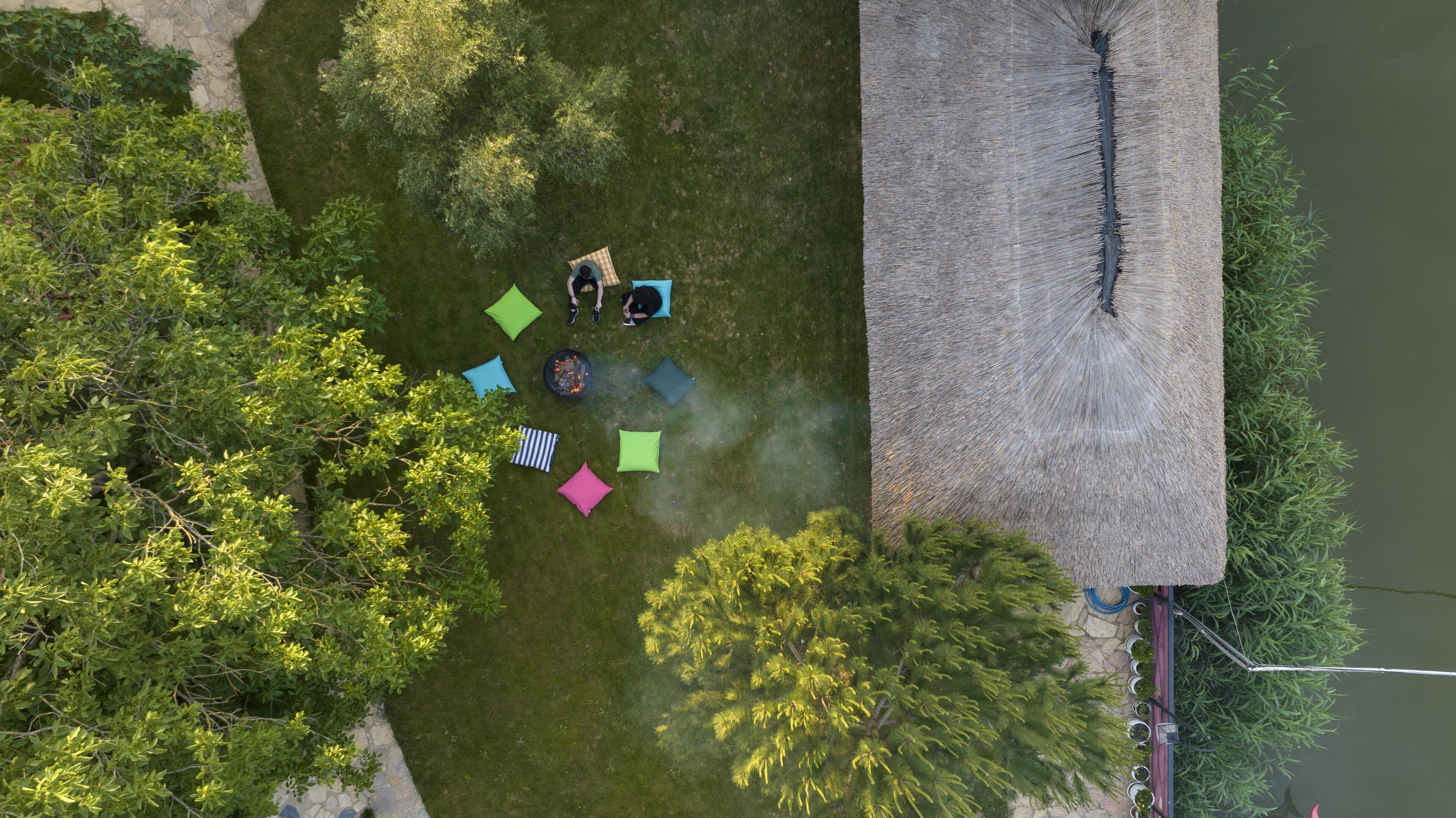 Vista aérea de un patio con un edificio de techo de paja, rodeado de abundante vegetación y un pequeño estanque.