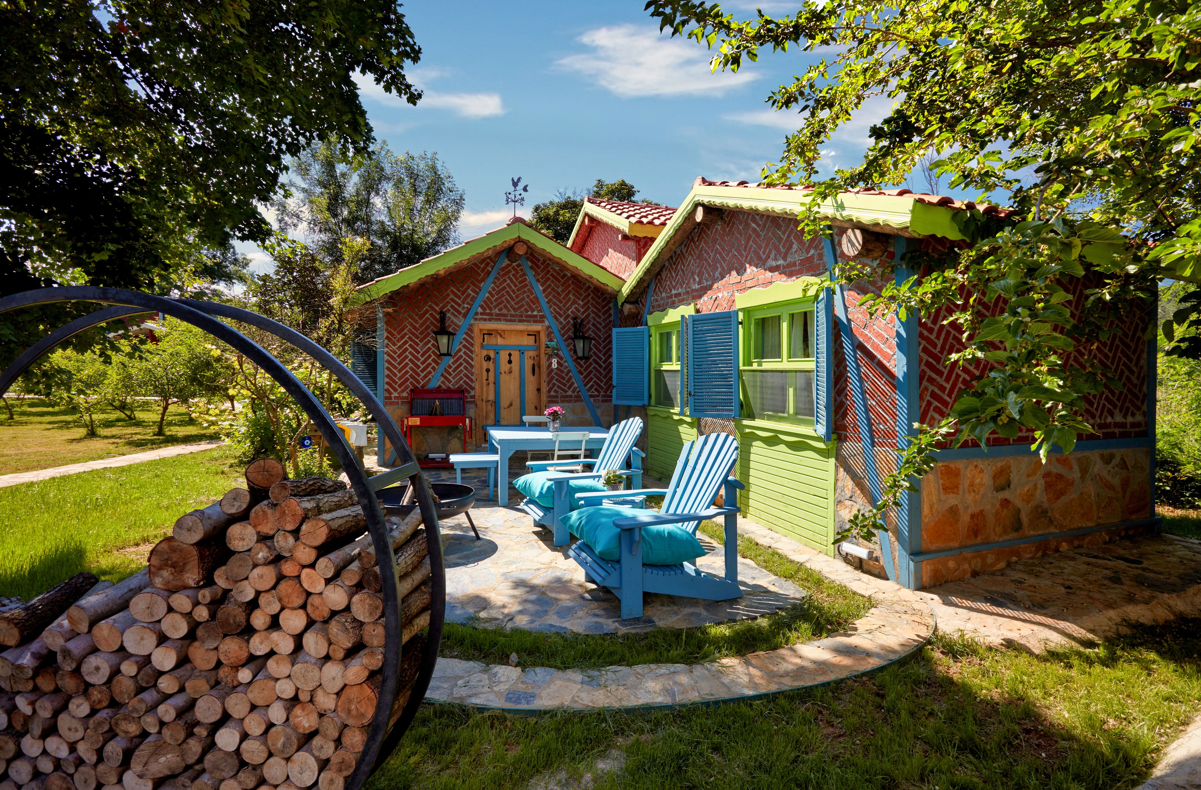 A rustic cabin with a stone patio, outdoor seating, and a stack of firewood.