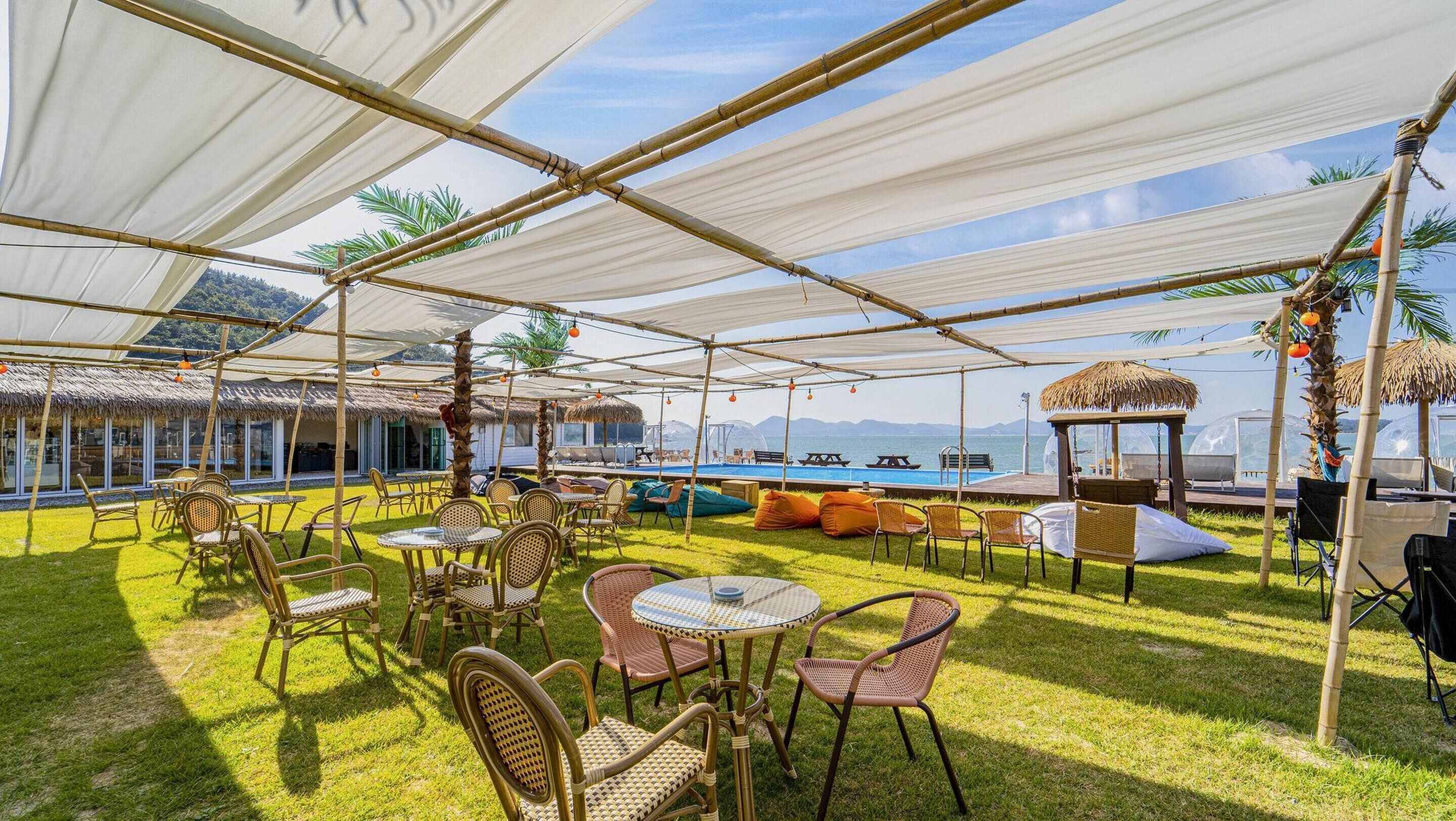 An outdoor seating area with tables and chairs, a pool, and a view of the sea.