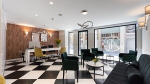Un moderno vestíbulo de hotel con piso de diseño ajedrezado, mobiliario verde y negro, y amplias ventanas que ofrecen vistas a la calle.