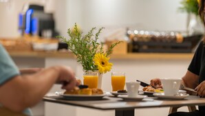 Un desayuno con una mesa, un florero con una flor amarilla y una cafetera al fondo.