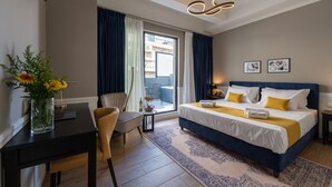 Habitación de hotel con cama, escritorio, silla, un florero con flores y vistas al exterior.