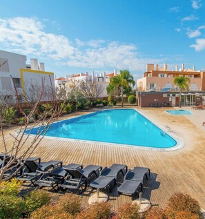 Ein Swimmingpool mit Liegestühlen, umgeben von Gebäuden und Grünflächen.