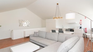 A modern living room with a grey sectional sofa, a white coffee table, and a kitchen in the background. - Convento das Bernardas Lux T2 (Tavira)