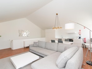 A modern living room with a grey sectional sofa, a white coffee table, and a kitchen in the background. - Convento das Bernardas Lux T2 (Tavira)