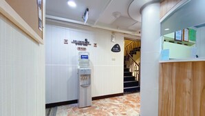 A hotel reception area with a water dispenser, a staircase, and a reception desk.