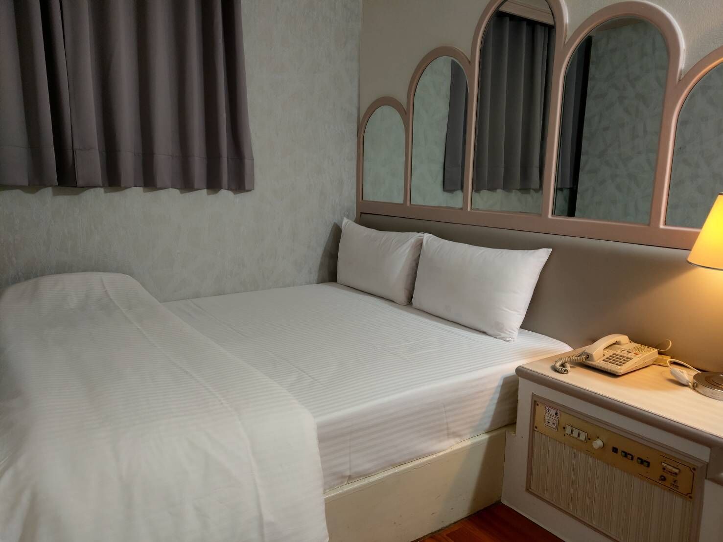 Habitación de hotel con cama, mesita de noche con teléfono y espejo sobre la cama.