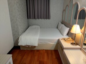 Una cama individual con colchón y almohadas blancos, una mesita de noche con lámpara y un teléfono pequeño.