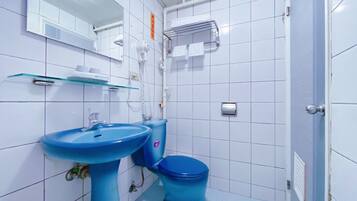 Ein Badezimmer mit weißen Fliesen, einem blauen Waschbecken, einer blauen Toilette und einem Glastregal.