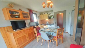 Une cuisine compacte avec des meubles de rangement en bois, une table à manger pour quatre personnes et un téléviseur posé sur un meuble en bois.