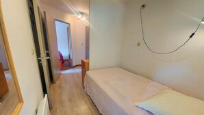 Une petite pièce propre, avec un lit simple, un plancher en bois et une porte donnant sur une autre pièce.