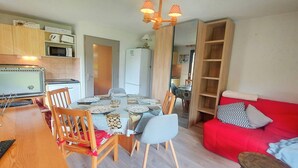 Un espace de vie compact comprenant un coin repas, une kitchenette et un canapé rouge.