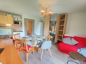 A compact living space with a dining area, a kitchenette, and a red sofa.