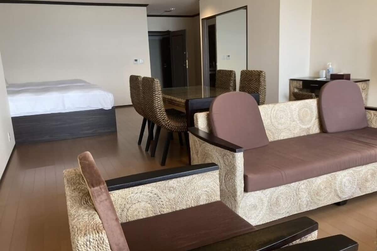 Moderni hotellihuone, jossa on sänky, sohva, ruokapöytä tuoleineen ja pieni sivupöytä.
