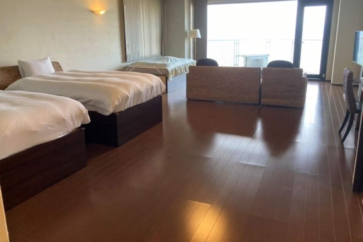 Hotellihuone, jossa on kolme sänkyä, parveke ja näkymä kaupunkiin.