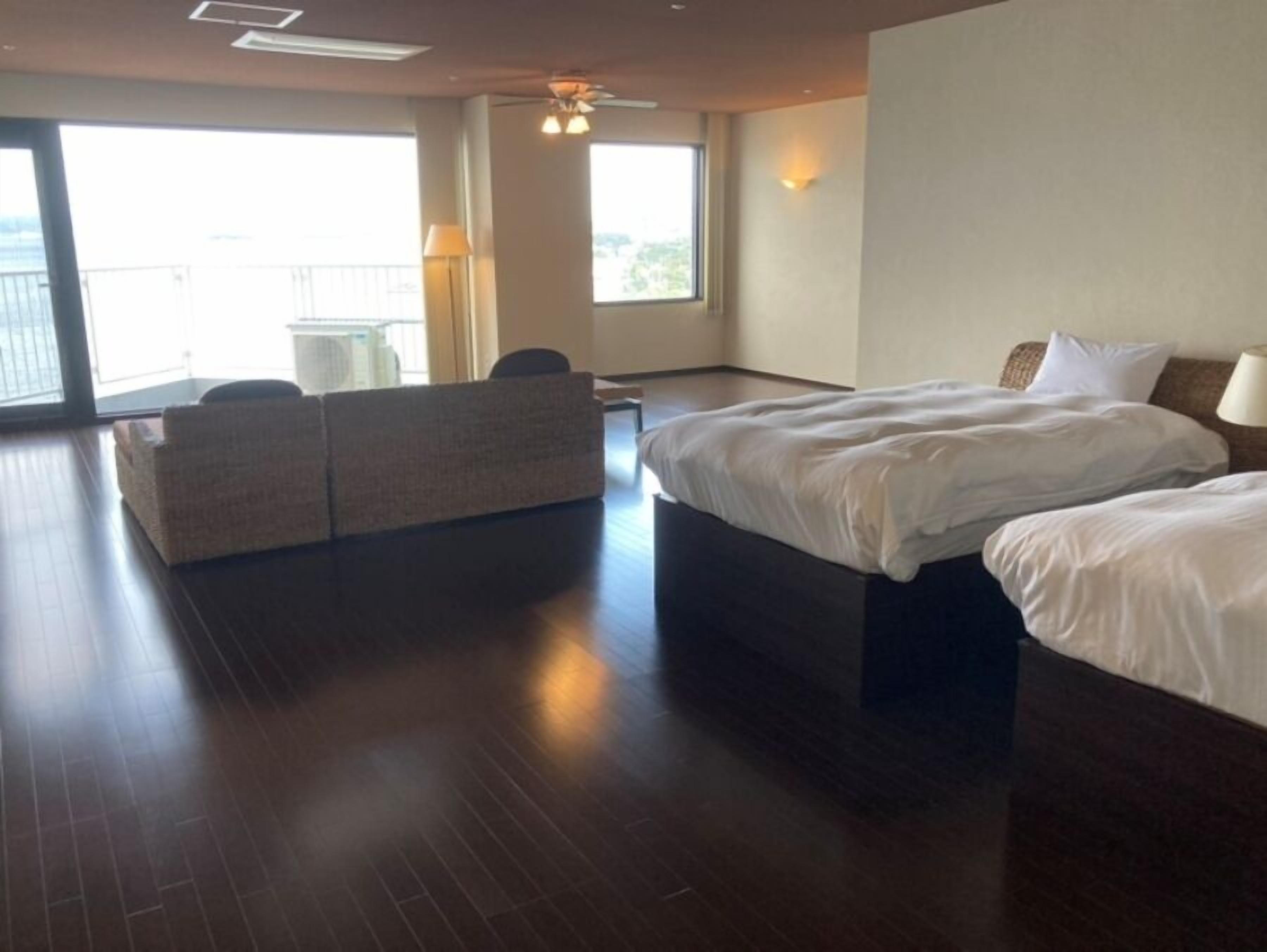 A hotel room with a large bed, a sofa, and a balcony.