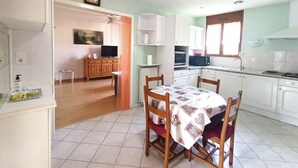 Une cuisine de taille réduite avec des meubles blancs, une table à manger avec des chaises, un ventilateur de plafond et une fenêtre avec des rideaux.