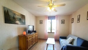Un salon avec un meuble en bois, un téléviseur, un ventilateur de plafond, une fenêtre avec des rideaux et un canapé bleu.