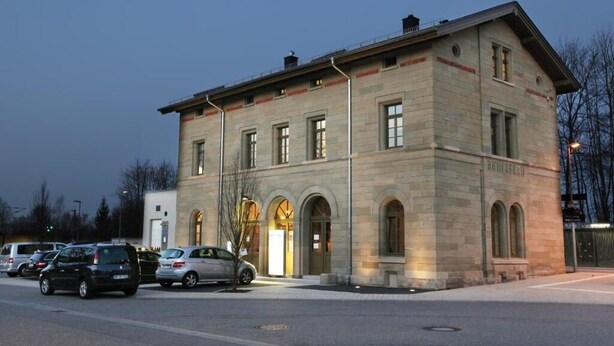 Ein Gebäude aus Stein mit Rundbogenfenstern und einer flachen Dachlinie, vermutlich ein öffentliches oder verwaltetes Gebäude.