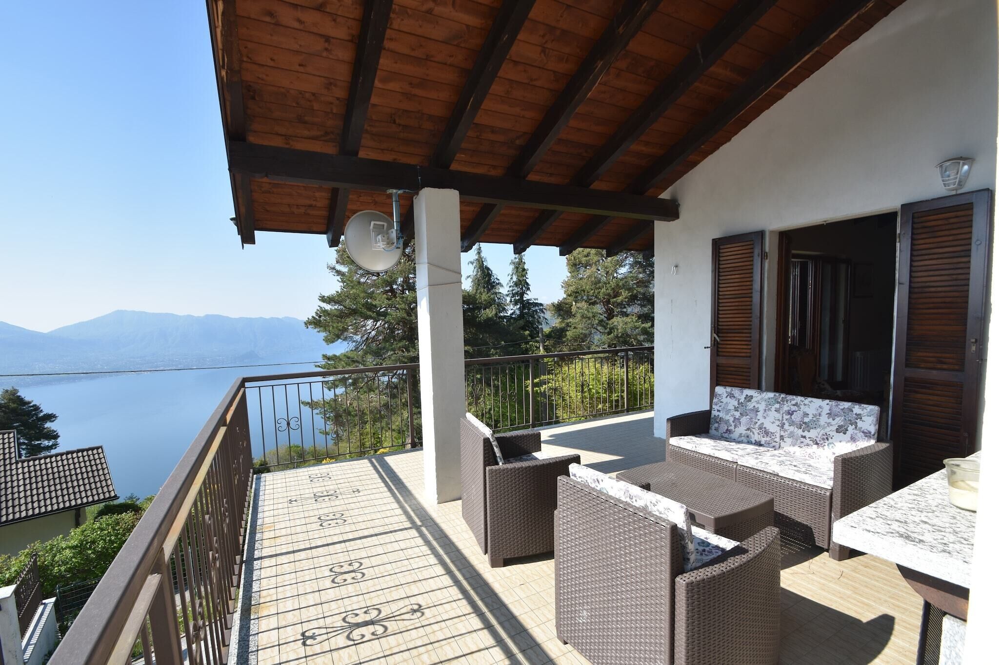 A balcony with wicker furniture, a view of a lake, and a mountainous landscape.