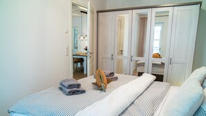 Ein Schlafzimmer mit Bett, Kleiderschrank und einem durchgehenden Türrahmen sichtbaren Badezimmer.