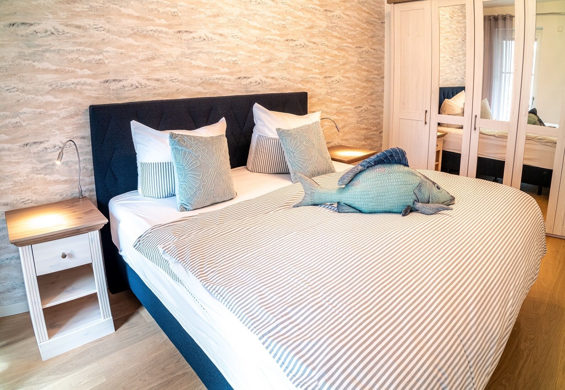 A bed with striped bedding, a headboard, and multiple pillows. There is a nightstand with a lamp on it.