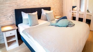 A bed with striped bedding, a headboard, and multiple pillows. There is a nightstand with a lamp on it. - Erdgeschosswohnung Dünen-residenz 11 im Ostseebad Wustrow (Ostseebad Wustrow)