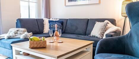 Een moderne woonkamer met een donkerblauwe bank, een houten salontafel en een ingelijste foto aan de muur.