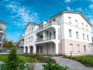 A multi-story residential building with balconies, a garden area, and a clear blue sky.