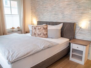 A neatly made bed with striped bedding, a headboard, and two bedside tables with drawers.